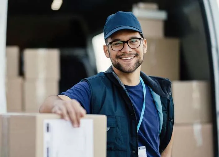 Person in a cap and vest beside cardboard boxes at the open rear of a van
